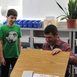 A Room 5 student shows his visitor his classroom and desk